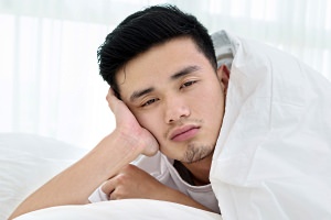 Asian man awake in bed with sleepy eyes.