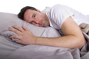 Man awake laying in bed on his side